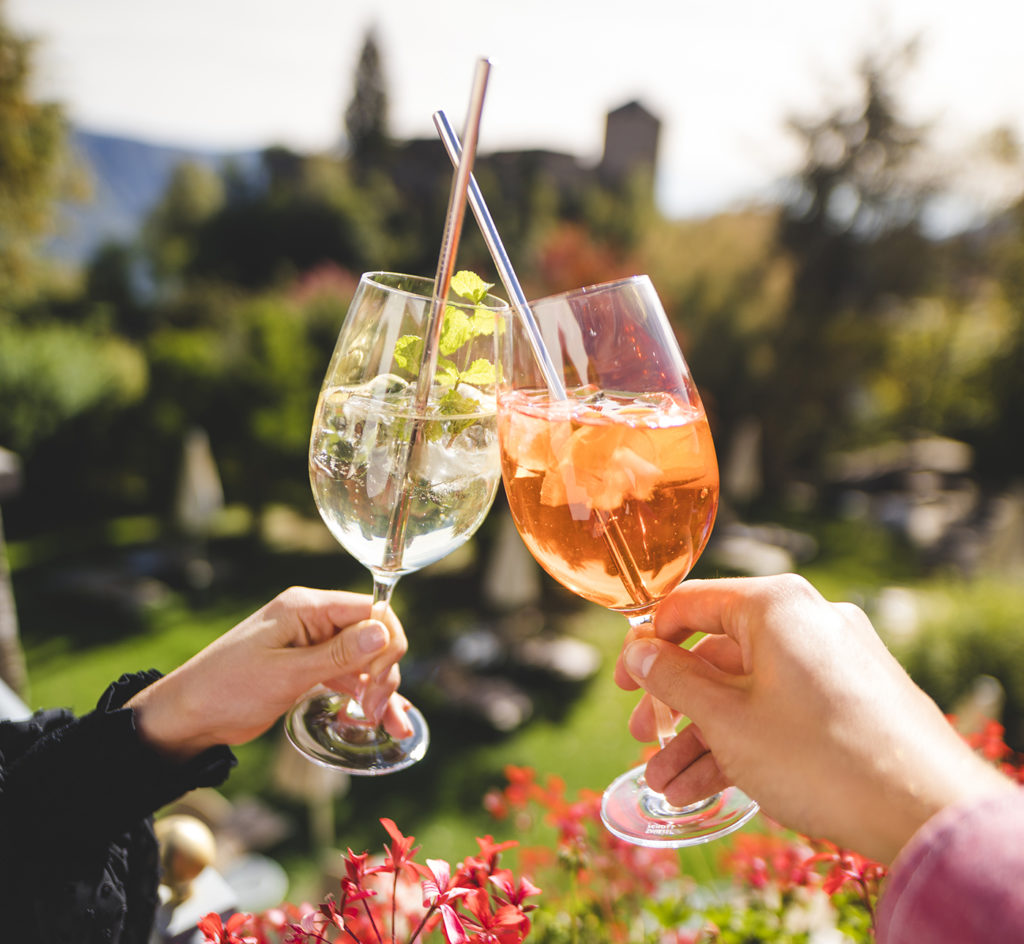 Zwei Hände halten je ein Glas Hugo und Veneziano und stoßen gemeinsam auf einer Terrasse an - 10 Dinge über Südtirol